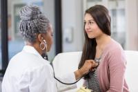 doctor in white coat holding stethoscope on chest of teenage girl